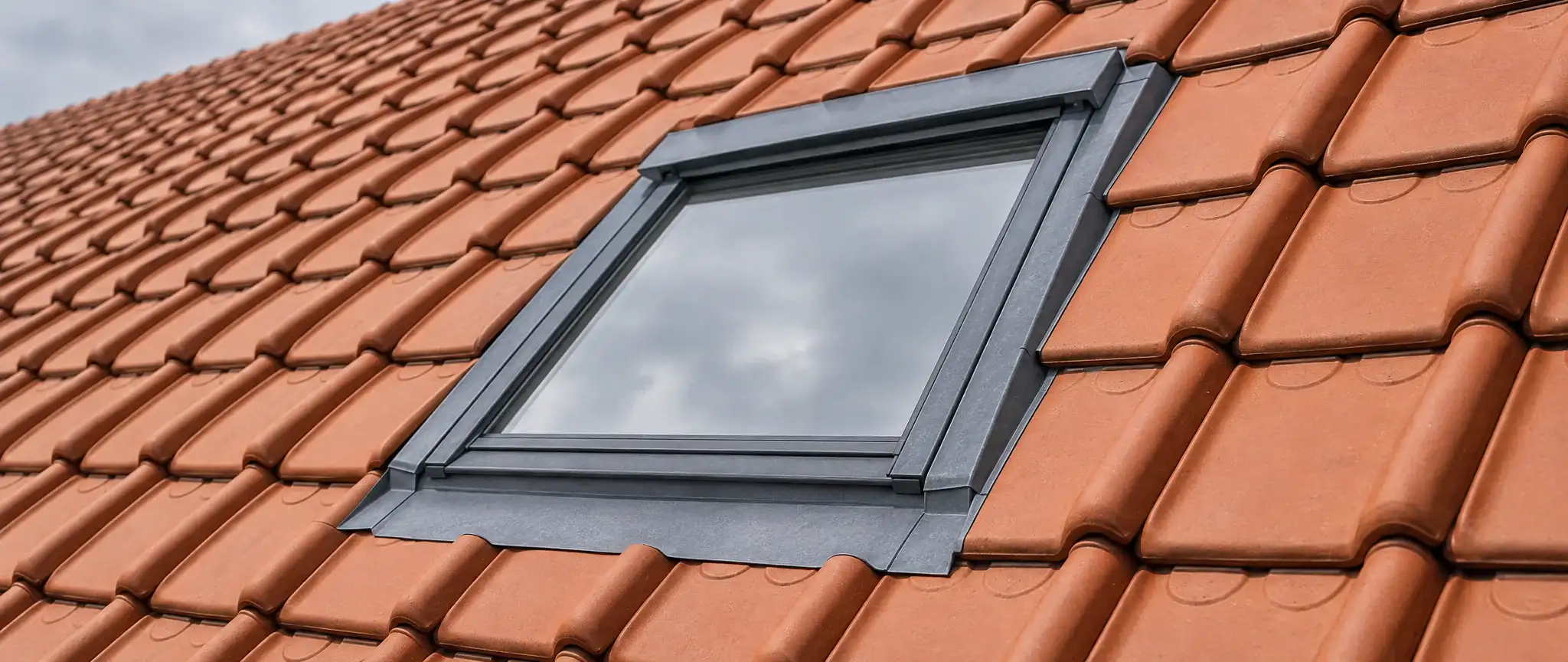 Couvreur à Gravelines : fenêtre de toit encadrée de zinc dans une toiture de tuiles à emboîtement