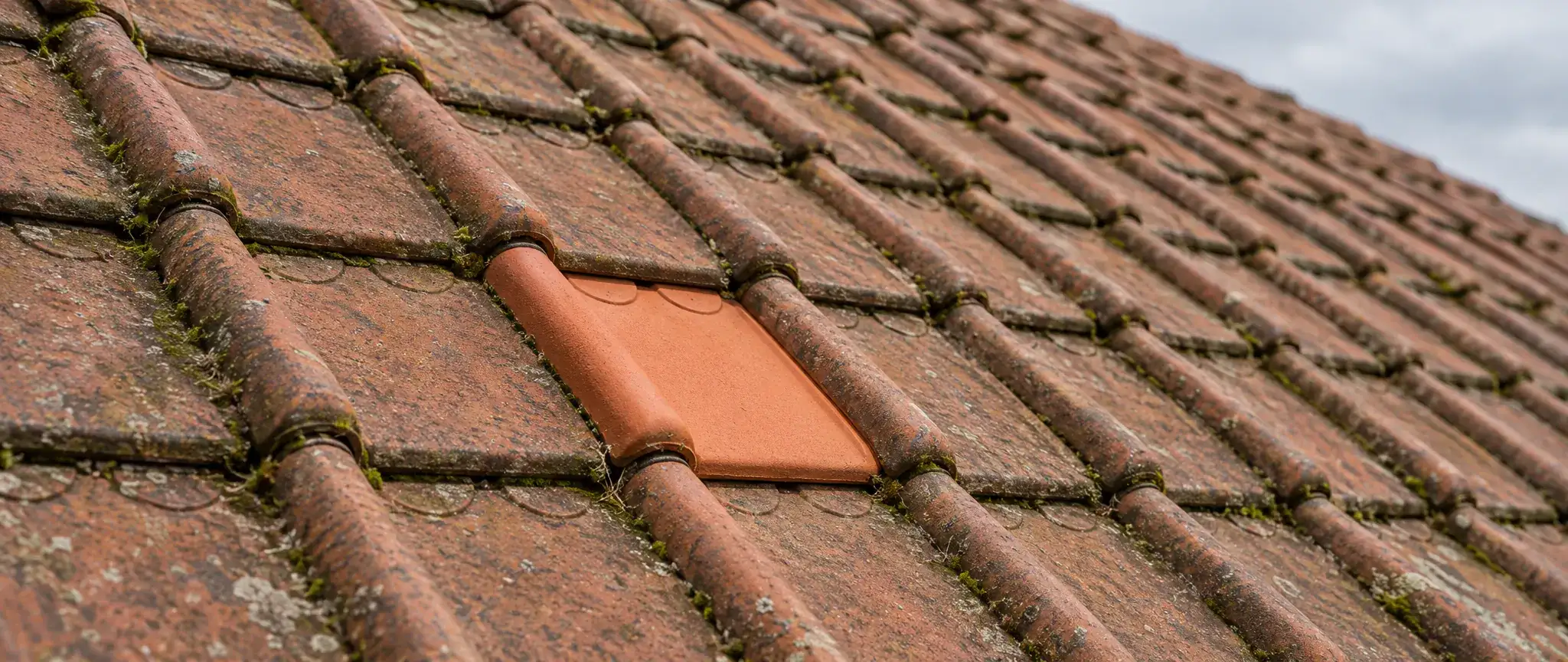 Réparation de toiture à Dunkerque : tuile neuve remplacée au milieu de tuiles à emboîtement patinées